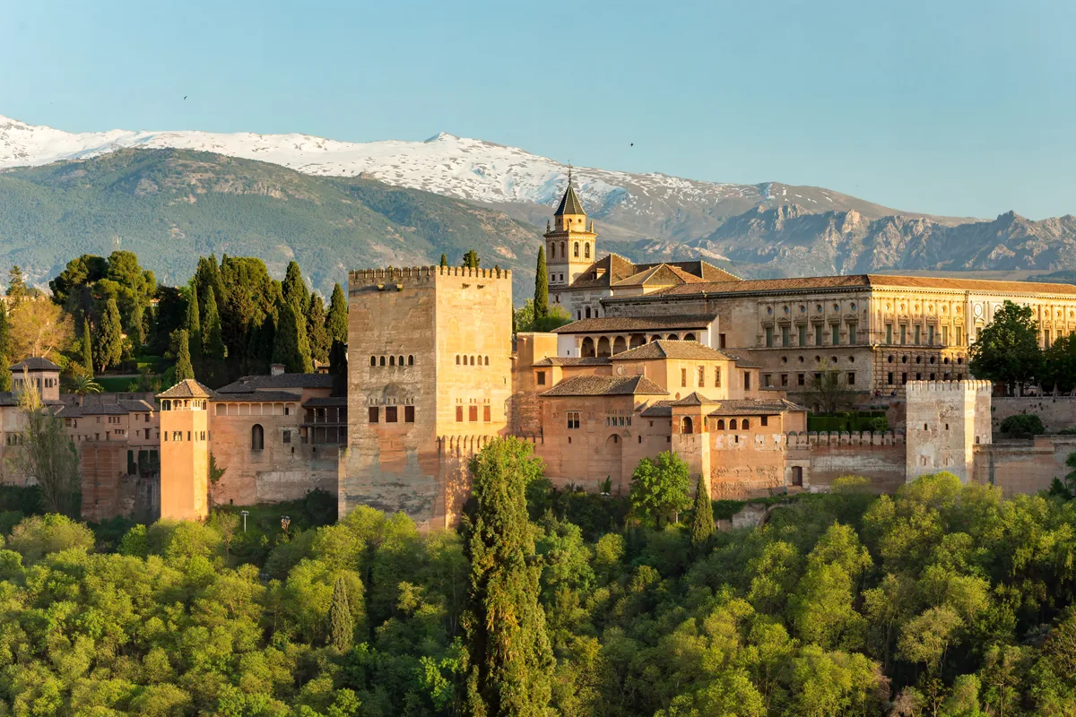 Die Alhambra in warmem Abendlicht vom Mirador de San Nicolás aus gesehen, mit der schneebedeckten Sierra Nevada im Hintergrund